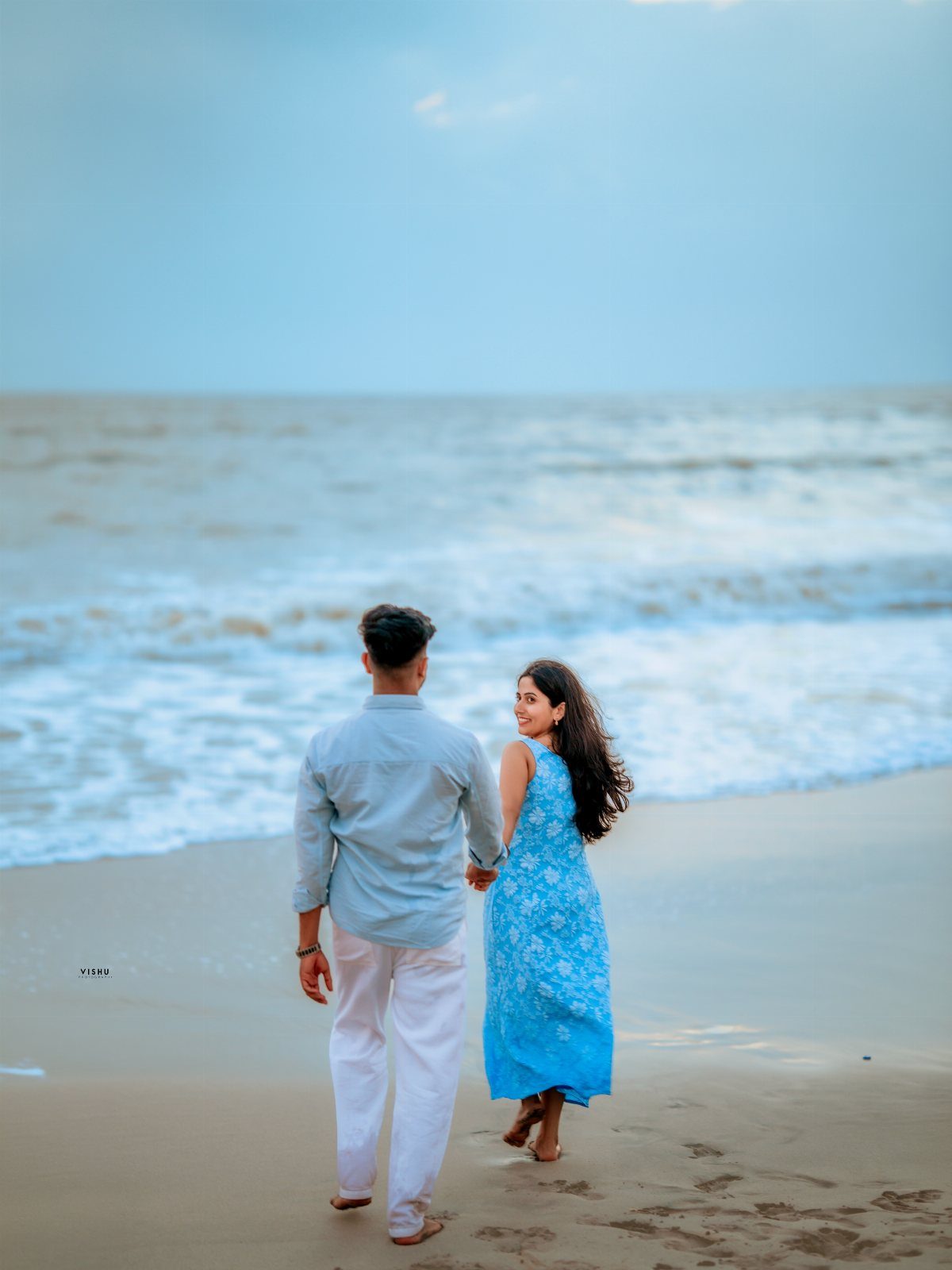 Couple walking hand-in-hand on a sandy beach by the ocean waves.