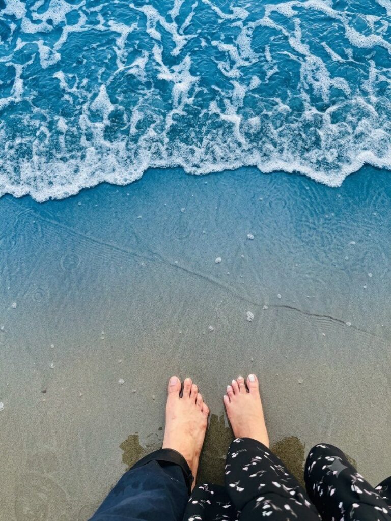 Two pairs of bare feet standing on wet sand as ocean waves approach.