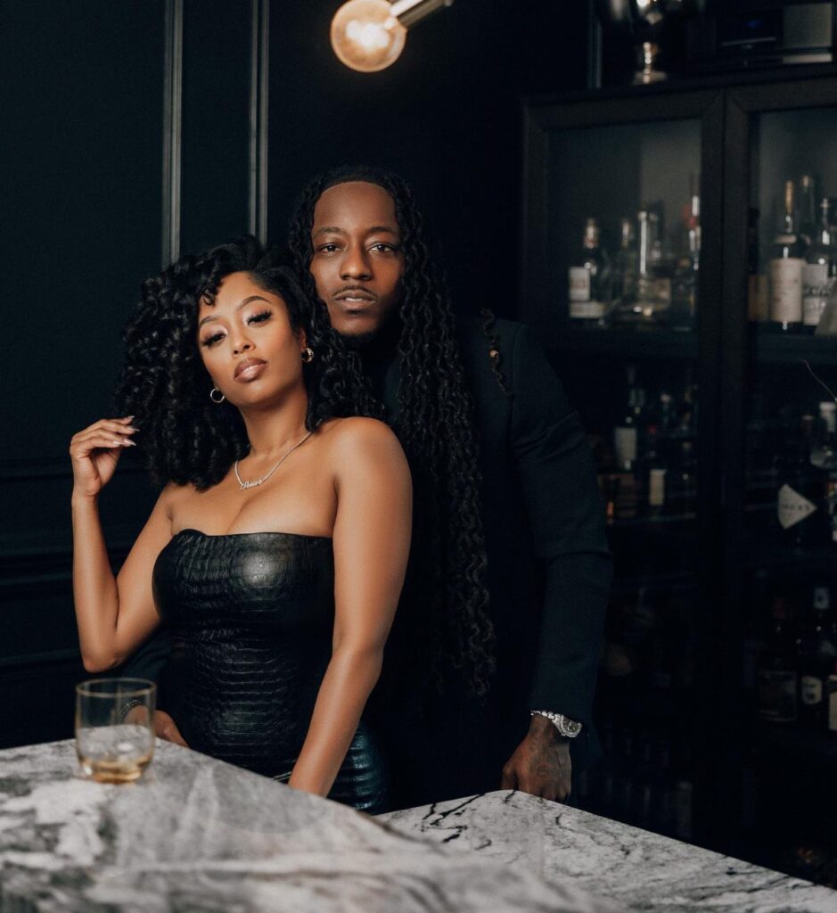 Black couple posing elegantly in a dark bar setting with a marble counter.
