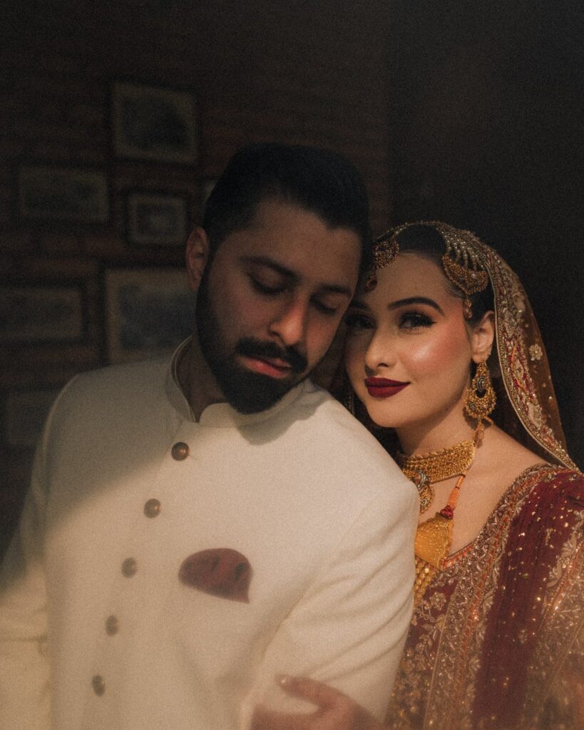 Bride and groom in traditional South Asian wedding attire posing closely together indoors.