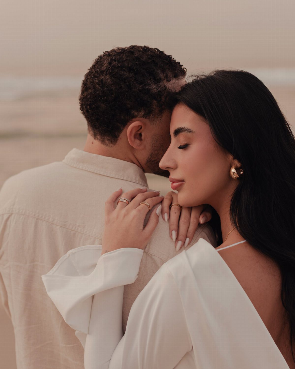 Couple embracing closely on a beach, woman resting head on man's shoulder.