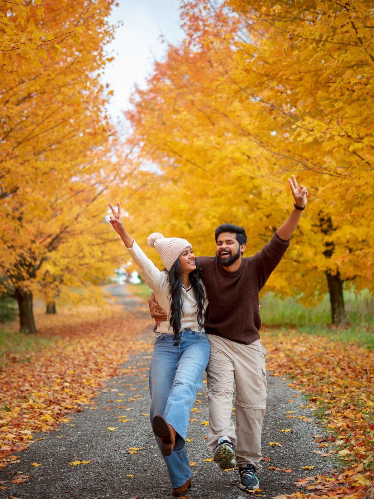 Smiling couple in autumn clothes posing on a path with yellow fall foliage