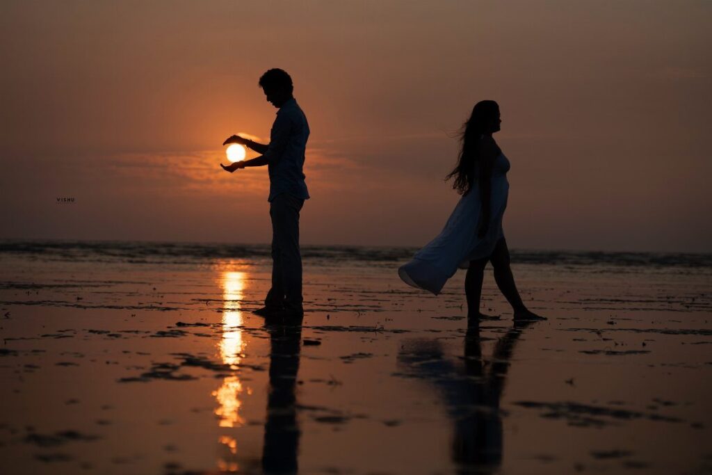 Silhouetted couple on a beach at sunset with man holding the sun.