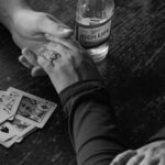 Hands with an engagement ring resting on a table with beer and cards.