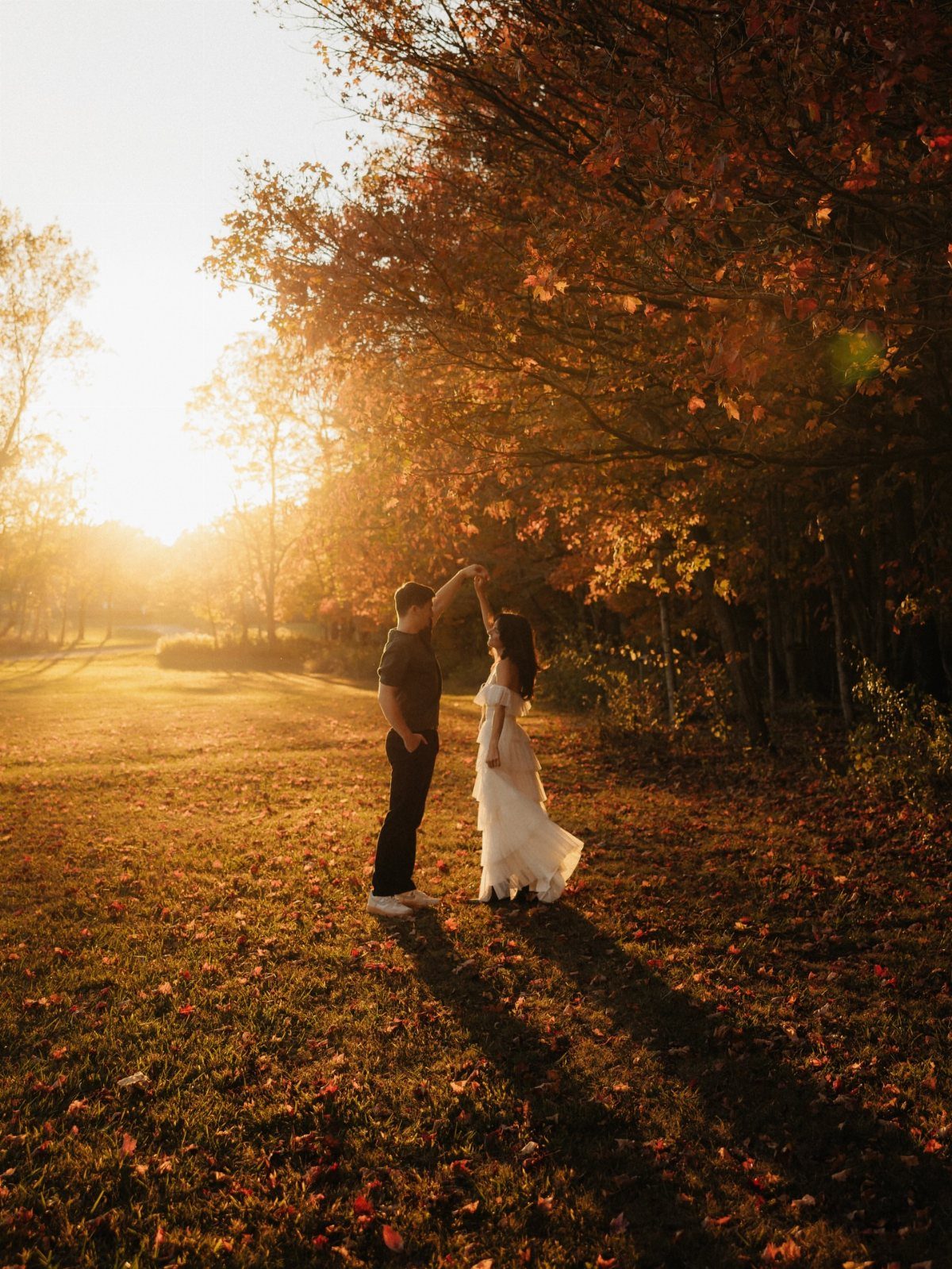 Couple posing in a field with autumn leaves, woman wearing a white dress.