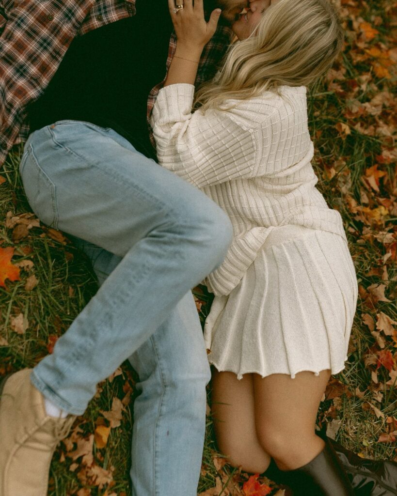 Couple in fall outfits embracing on a bed of autumn leaves and grass.