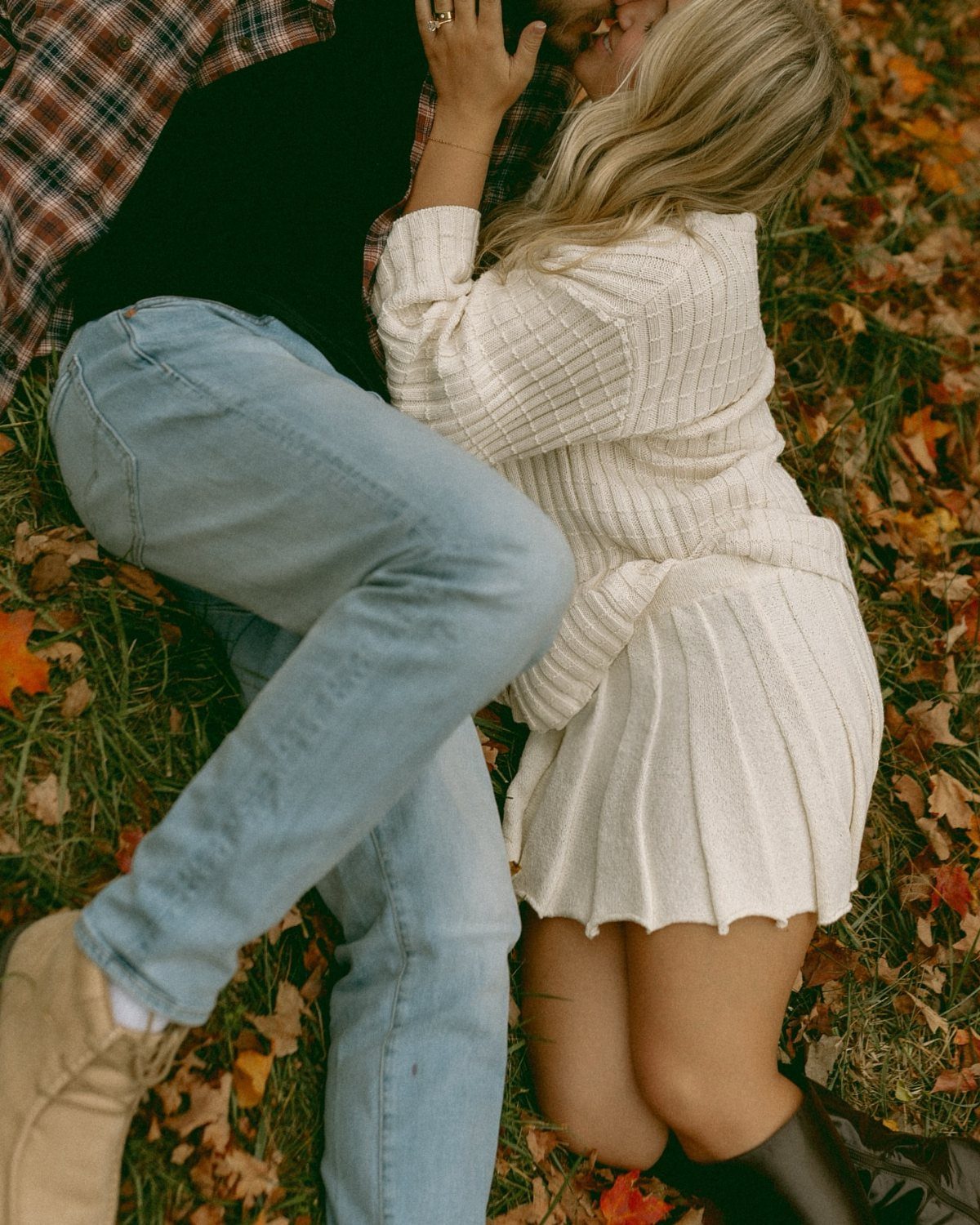 Couple in fall outfits embracing on a bed of autumn leaves and grass.