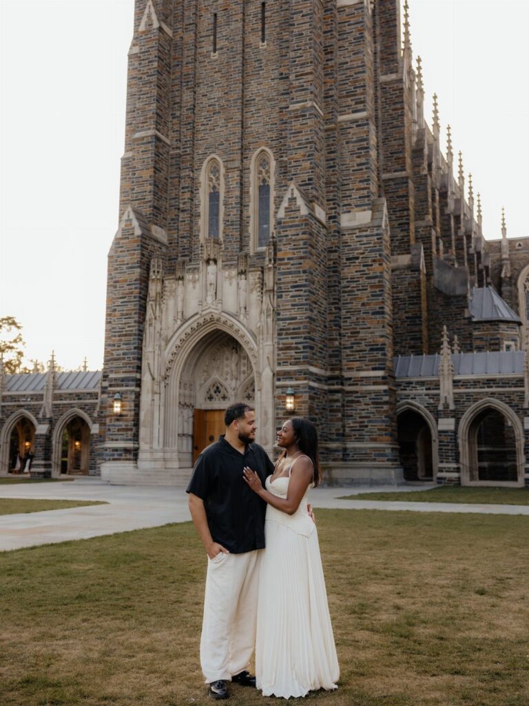 Couple posing in front of a gothic stone cathedral for engagement photos.