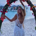 Woman in white sheer lace maxi gown and floral crown on tropical beach