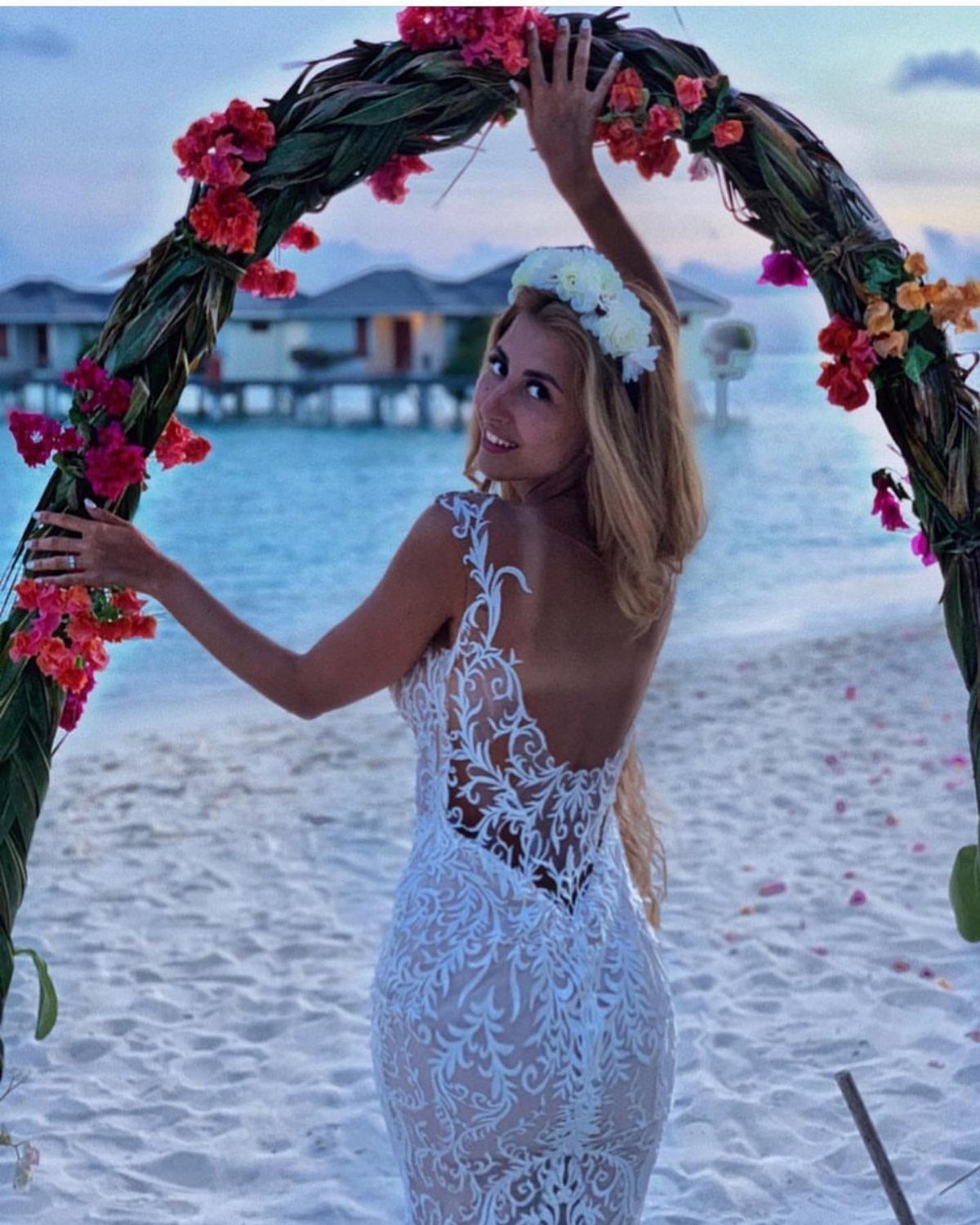 Woman in white sheer lace maxi gown and floral crown on tropical beach