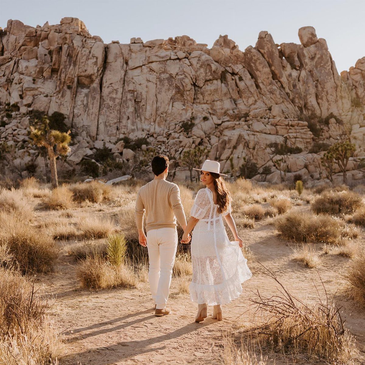 Couple holding hands walking through a desert landscape with large rock formations.