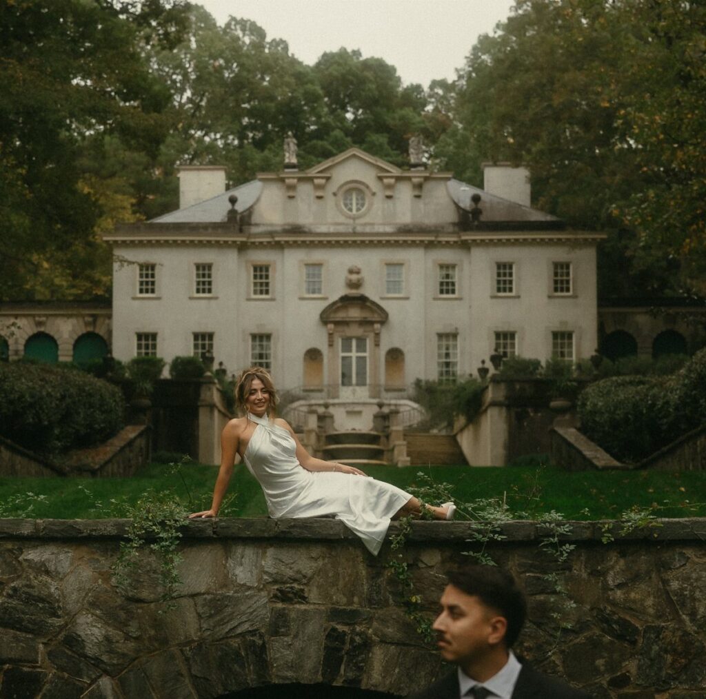 Woman in white dress posing on stone wall before a grand white estate