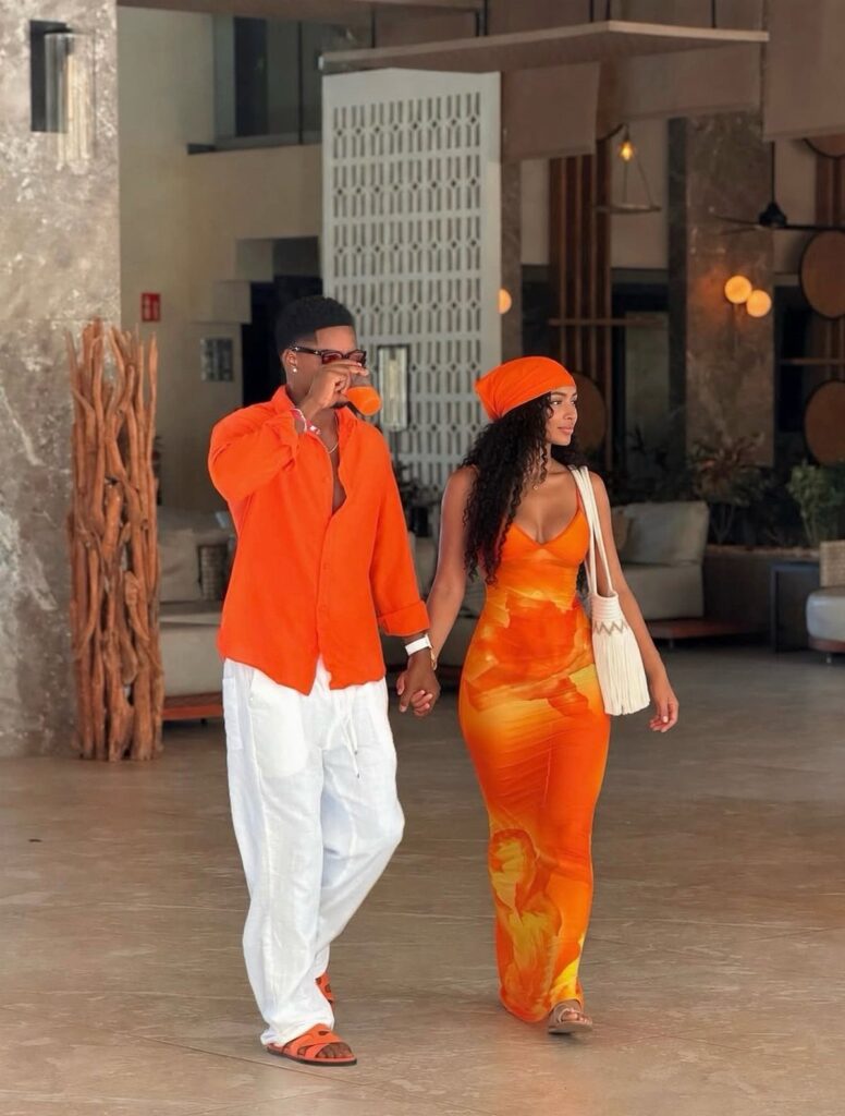 Couple walking hand in hand wearing matching bright orange outfits in a modern setting