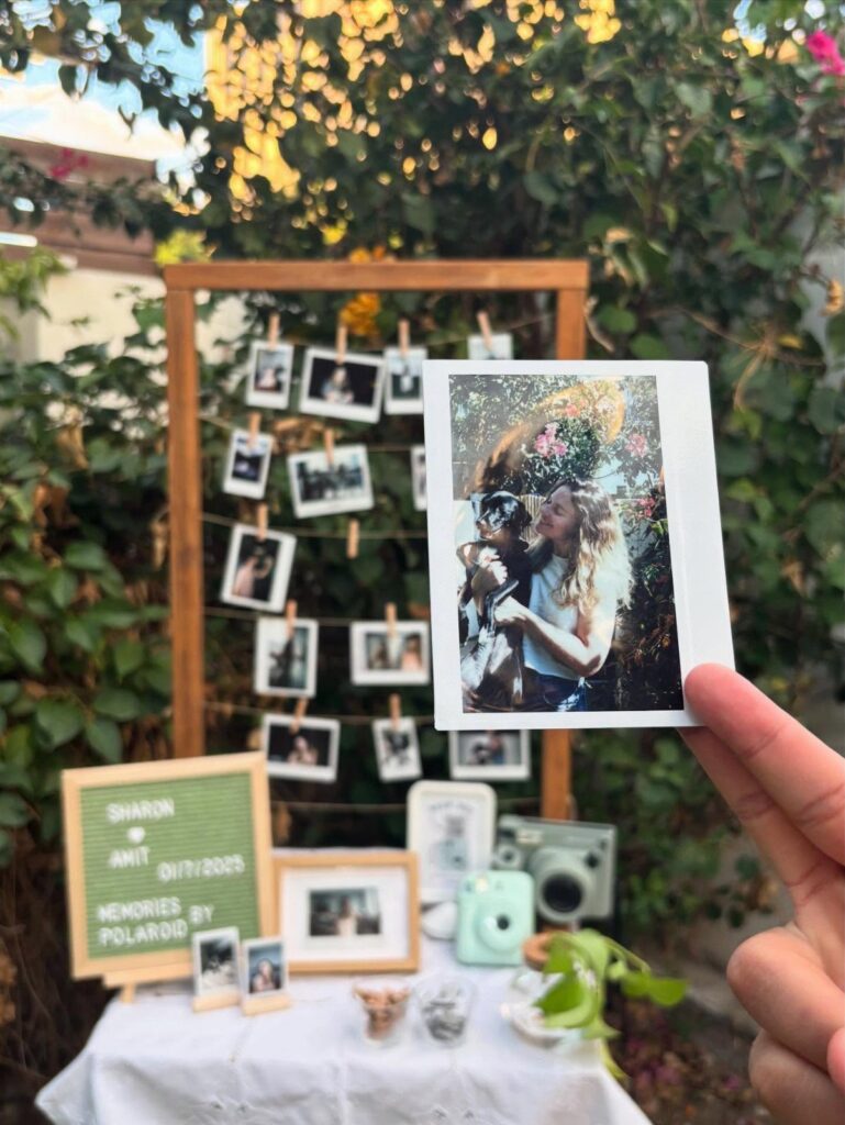 Hand holding a Polaroid photo in front of a wedding photo booth display.