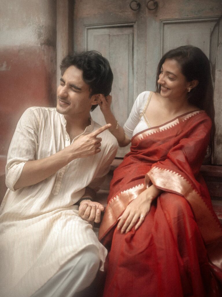 Couple in traditional Indian attire posing romantically against a rustic wall