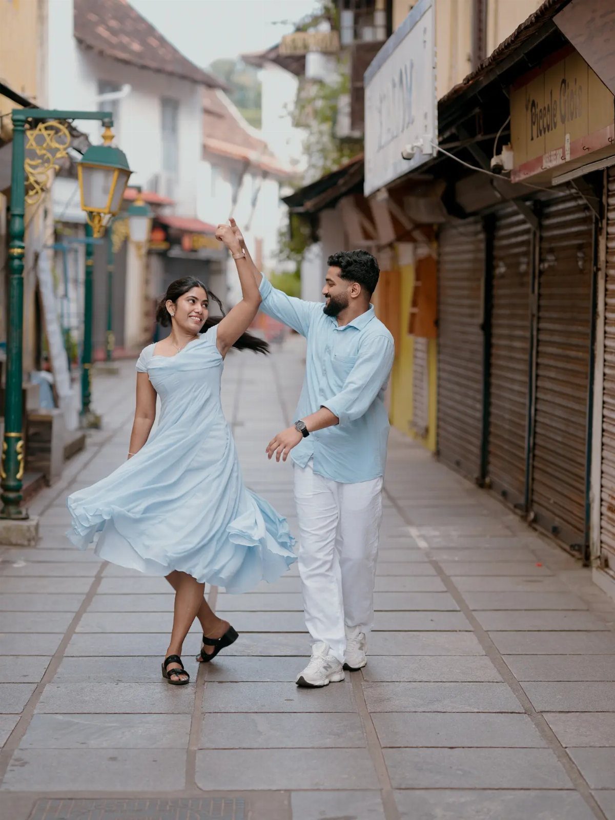 Couple dancing on a street wearing matching light blue and white outfits.