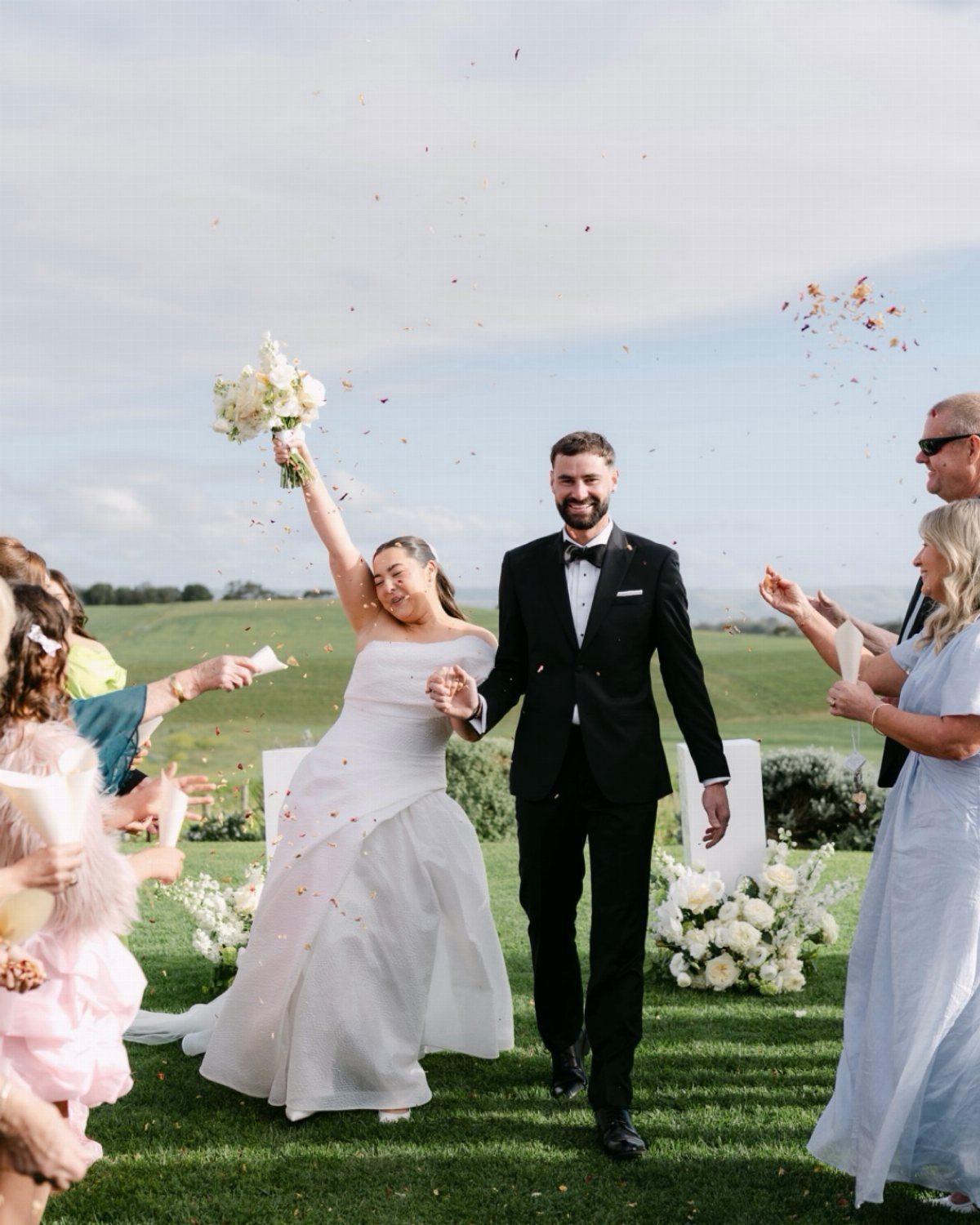 Bride and groom walking through guests throwing petals during an outdoor wedding celebration