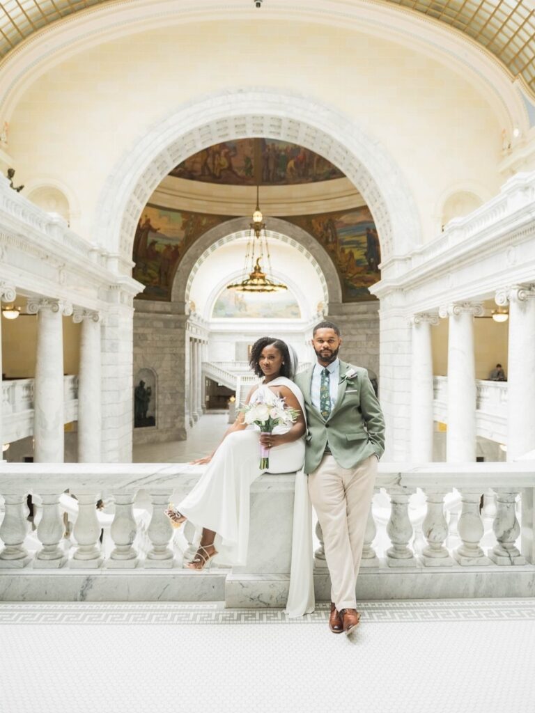 Bride and groom posing in a grand white marble hall with arched ceilings.