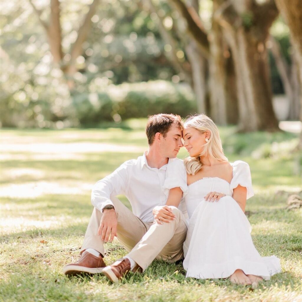 Couple in white spring outfits sitting on grass in a sunlit park