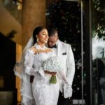 Bride in lace gown and groom in white tuxedo posing for an intimate portrait.
