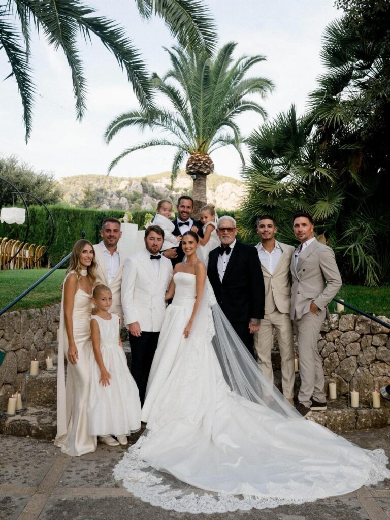 Bride and groom posing with their immediate family outdoors with palm trees behind them.