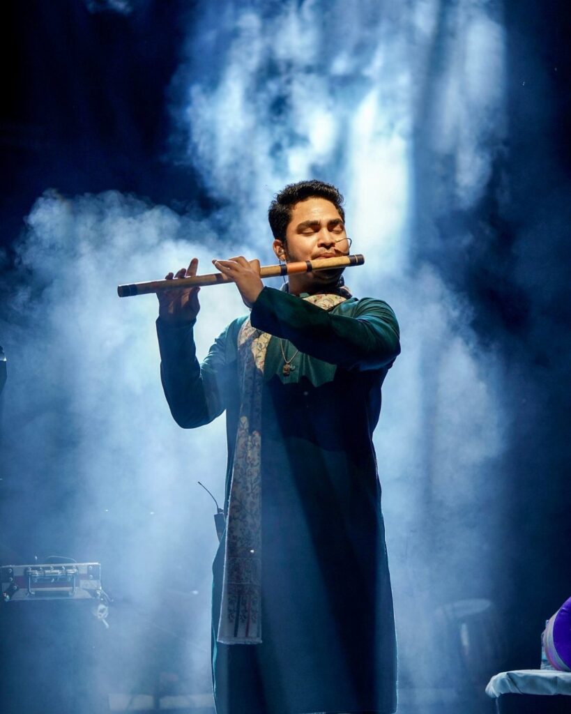 Man playing a wooden flute on a smoky stage with blue lighting