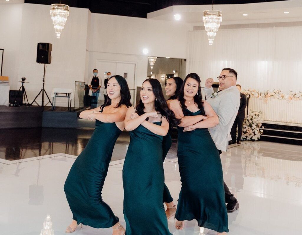Bridesmaids in green dresses and a groomsman dancing during a wedding party entrance.