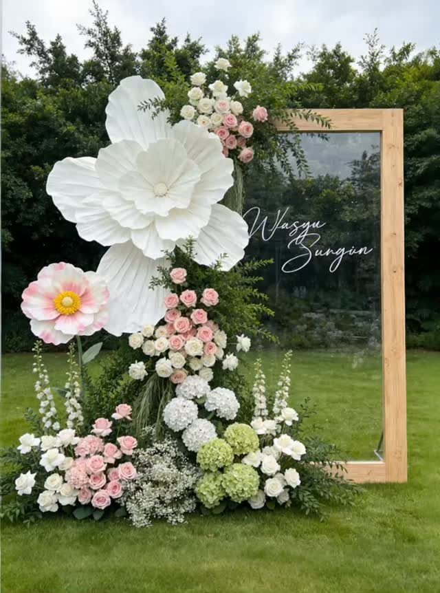 Wooden framed mirror decorated with large paper flowers and fresh floral arrangements outdoors
