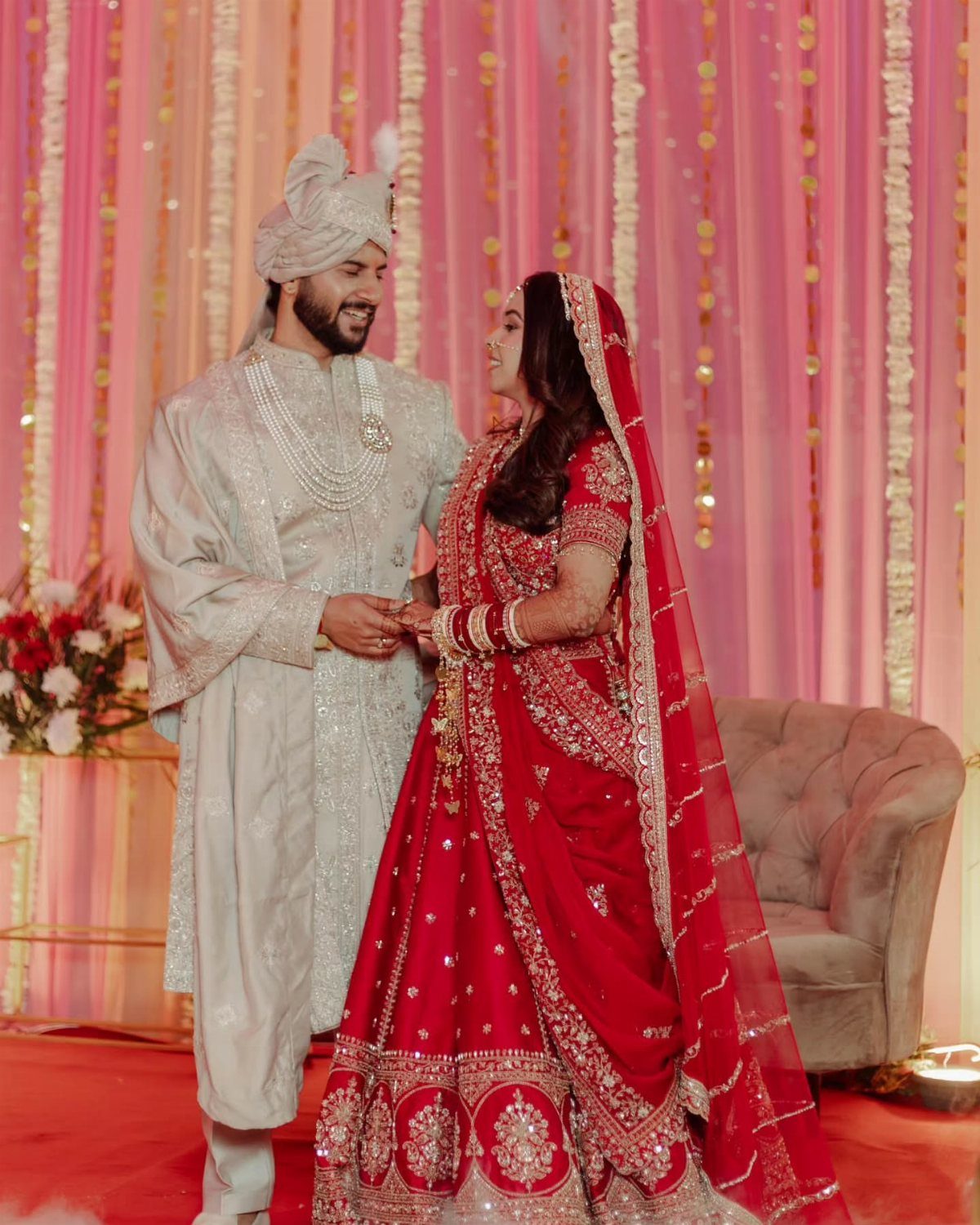 Bride in red lehenga and groom in silver sherwani holding hands at wedding