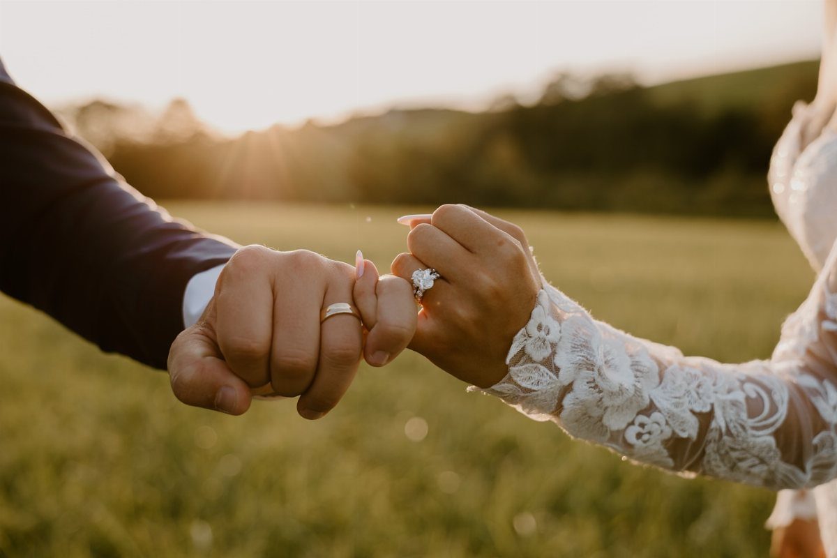 Couple's hands fist bumping in a field, showcasing their wedding and engagement rings.